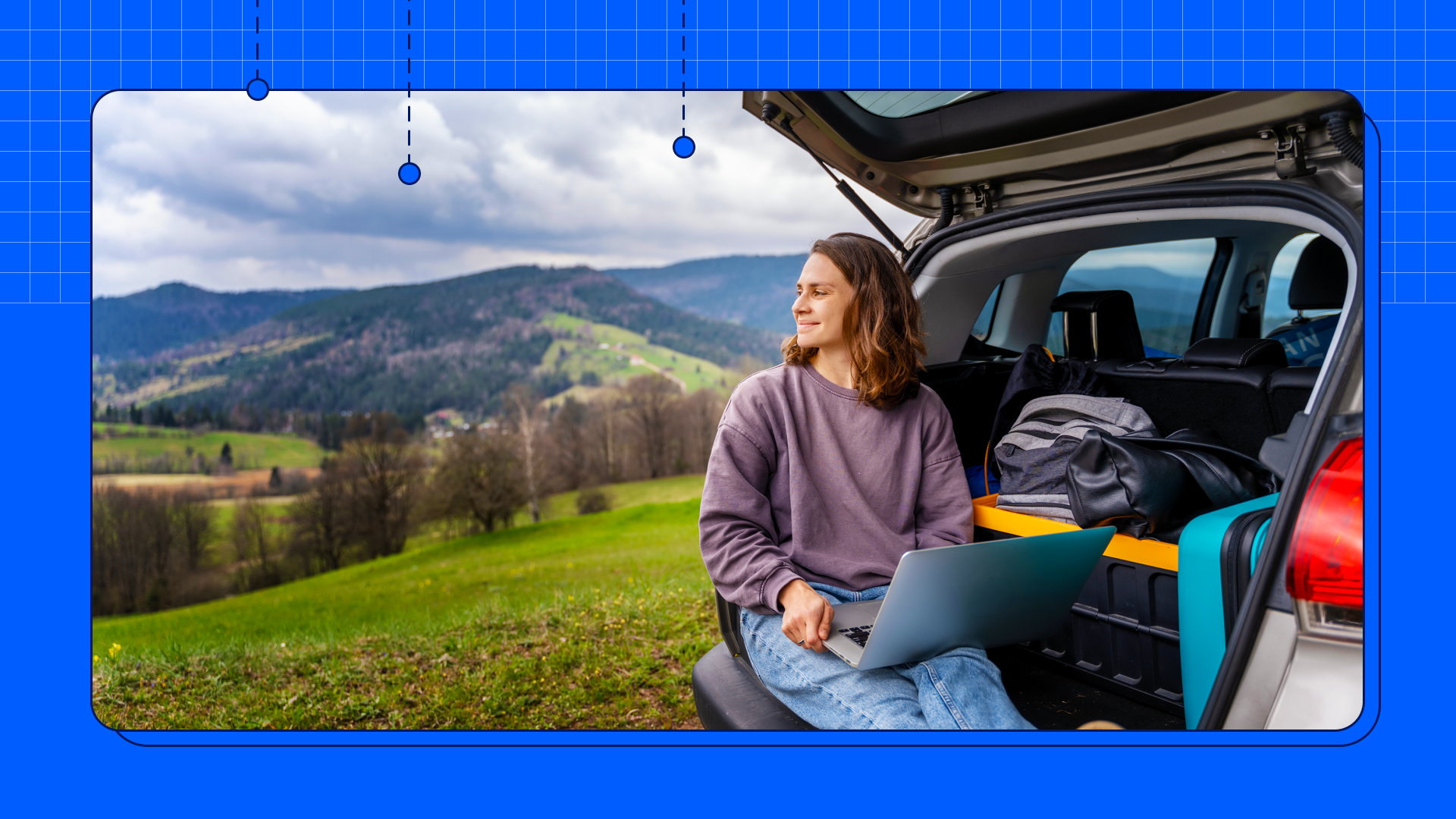 A woman working outside from the back of her hatchback car with a laptop in her hands